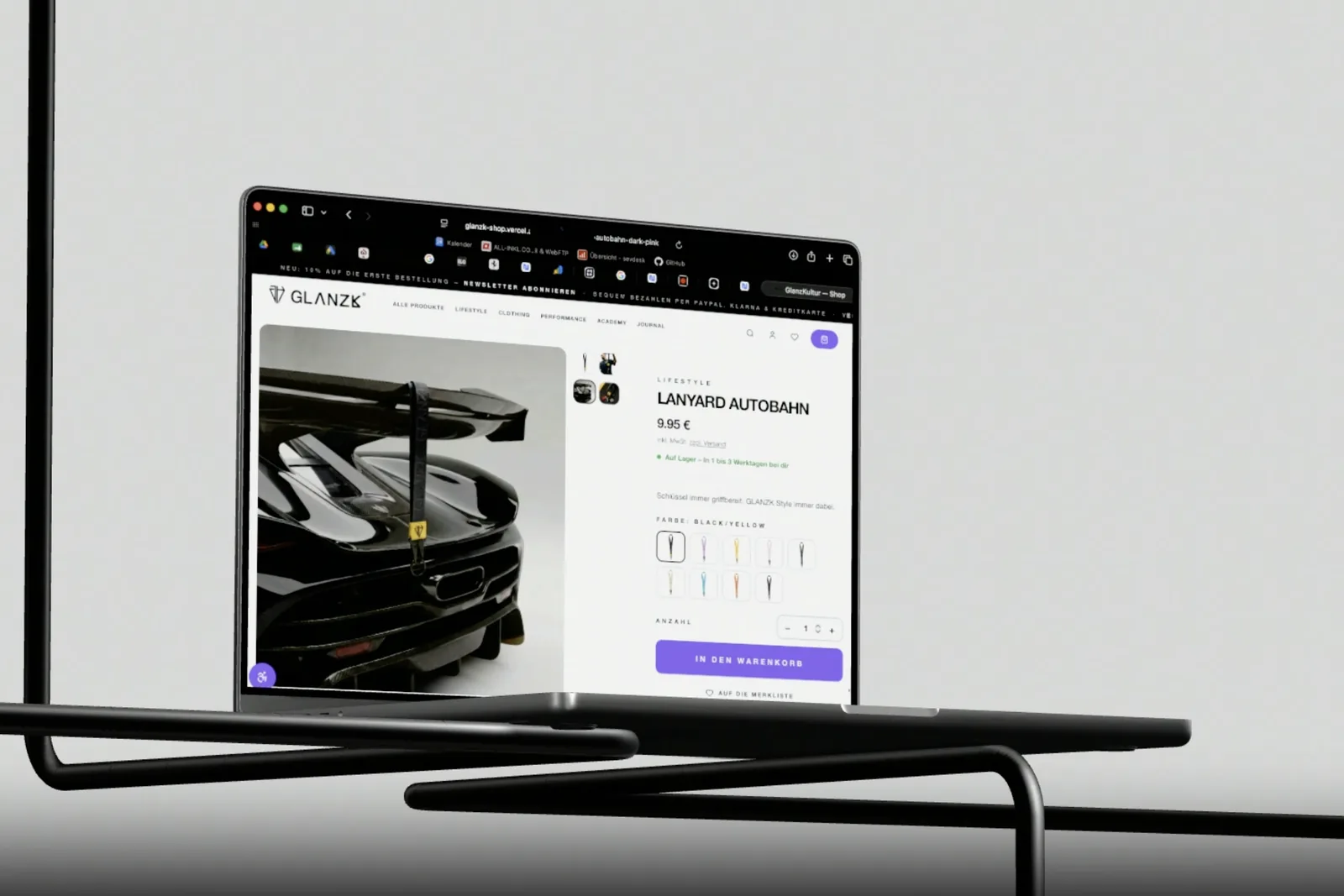 Eine Produktseite des GLANZK-Shops auf einem Notebook: ein Schlüsselband am Heckflügel eines Sportwagens, daneben Preis, Farbwahl mit zehn Varianten und die Schaltfläche „In den Warenkorb“.