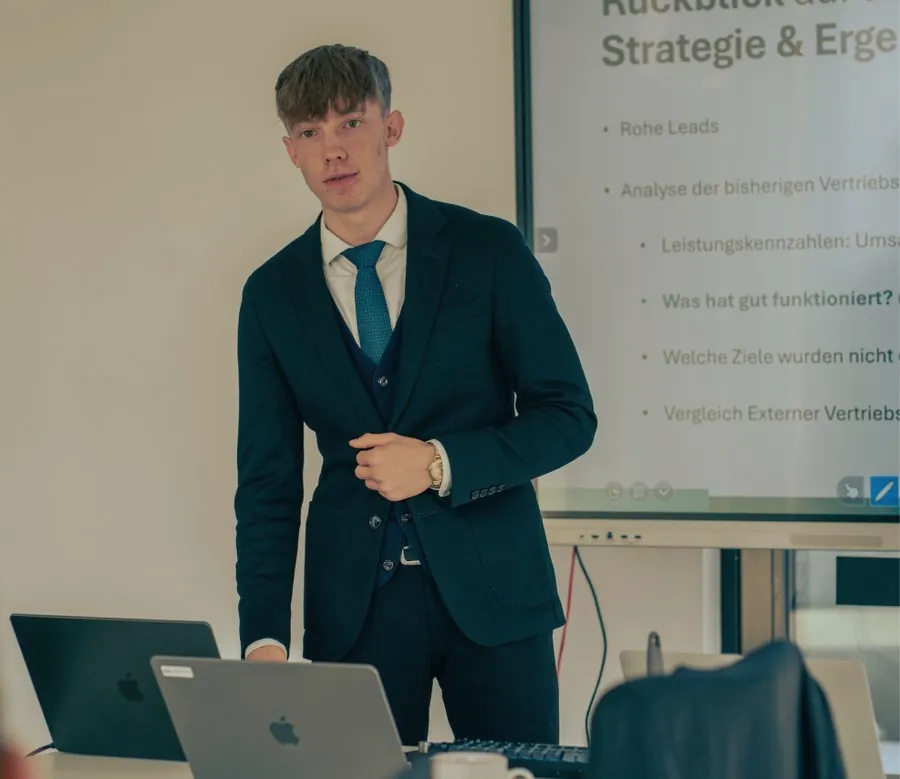 Vitali Sakun steht in einem Besprechungsraum vor einem Bildschirm mit einer Präsentation zu Strategie und Ergebnissen.