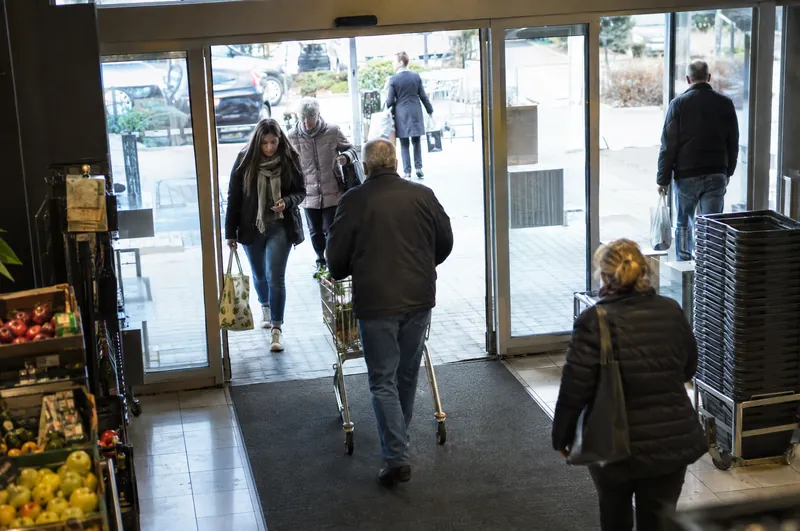 Blick von oben auf den Eingang eines Supermarkts, Menschen kommen und gehen.