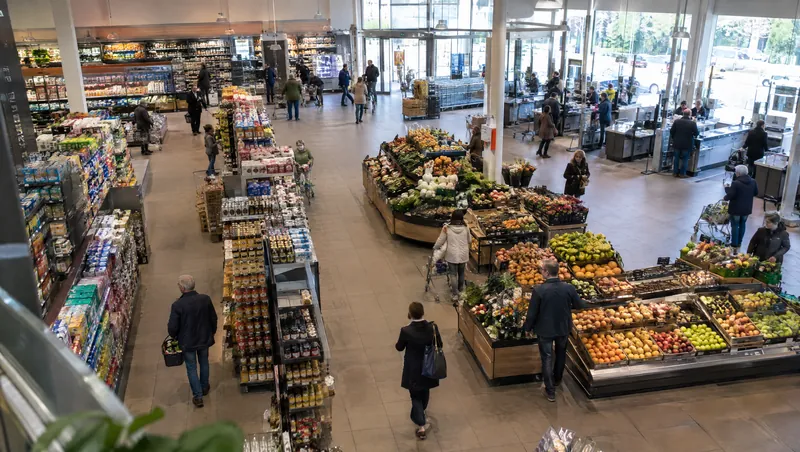 Weiter Blick von oben über die Verkaufsfläche eines Supermarkts mit Obstabteilung und Regalen.