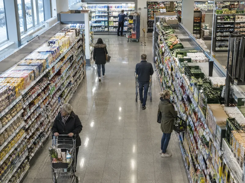 Blick von oben in den Hauptgang eines Supermarkts, mehrere Kundinnen und Kunden mit Einkaufswagen.