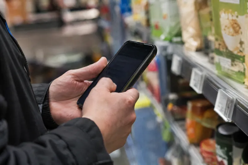 Eine Mitarbeiterin hält ihr Telefon neben die Preisleiste eines Regals.